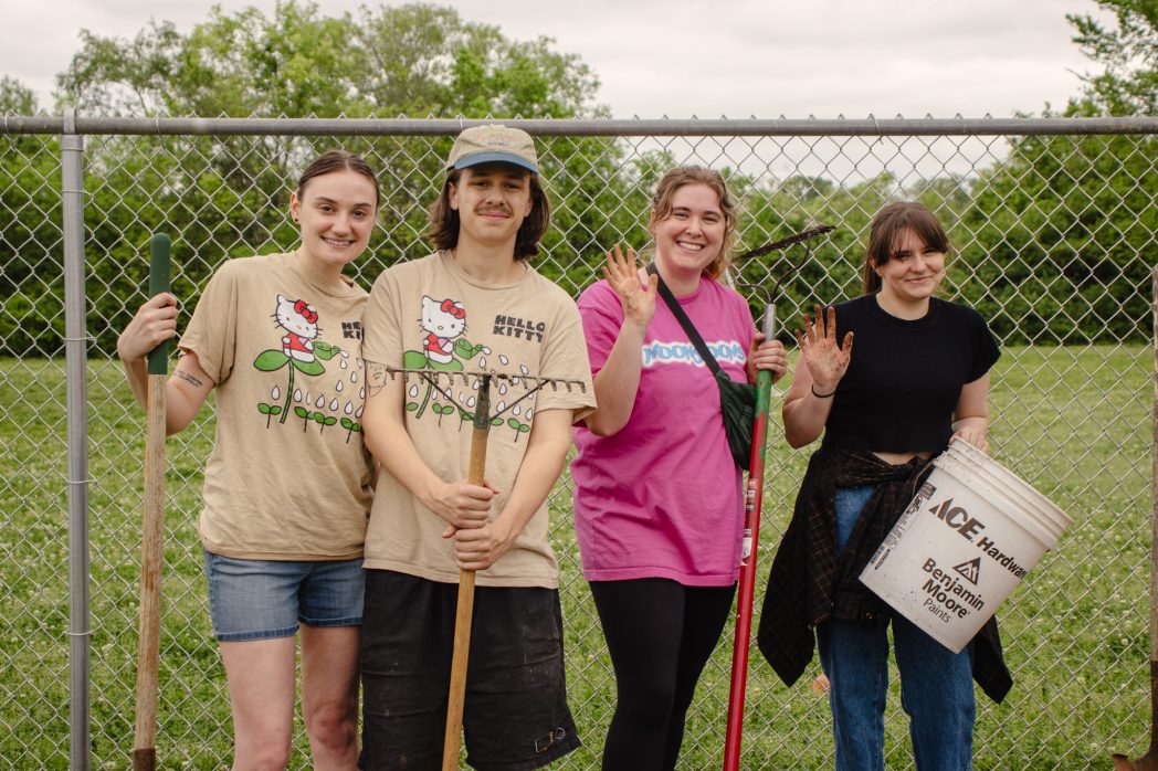 A group poses for a photo while holding gardening equipment