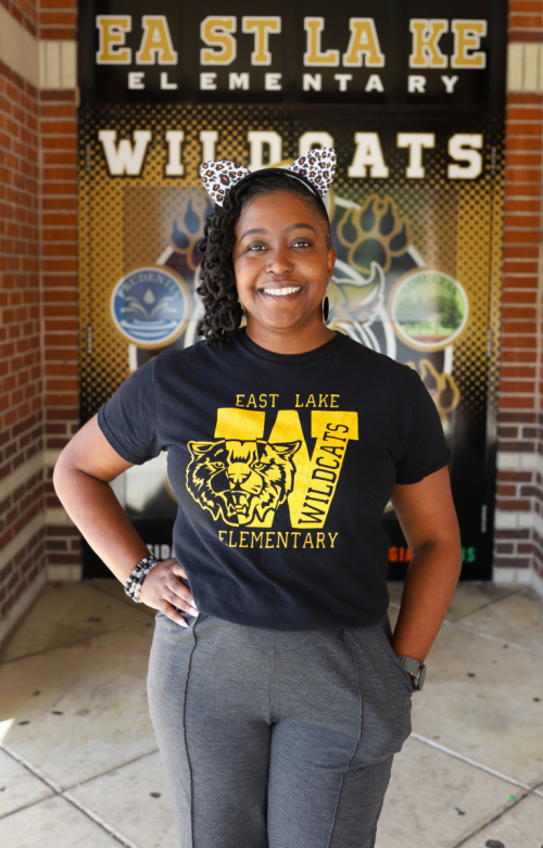 NEWSROOM COVER -  Dr. Jasmine Farrow Dr. Jasmine Farrow Principal at east lake elementary in front of school with ears on in east lake shirt