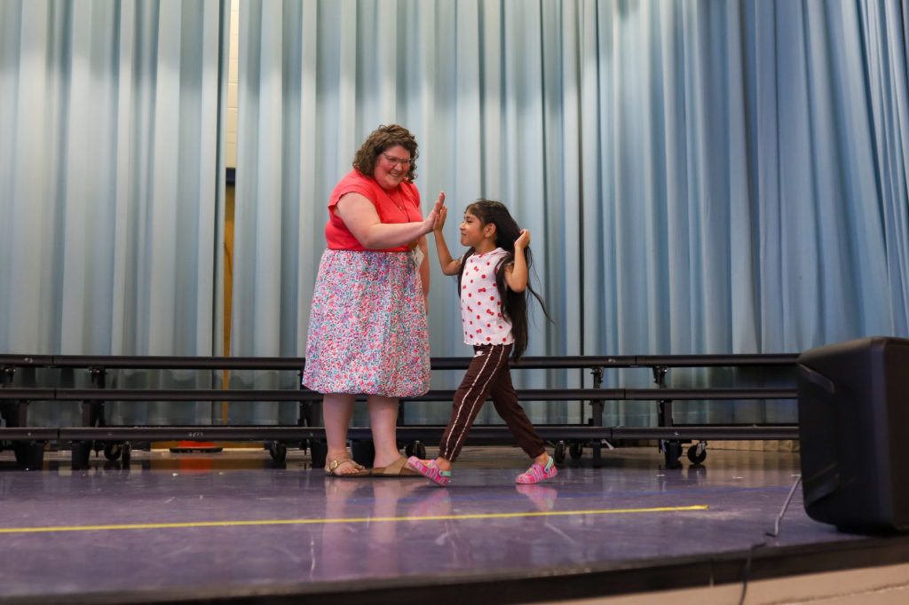 kindergarten, graduation, singing, stage, first year teacher, hug, group photo A woman gives a student a high-five